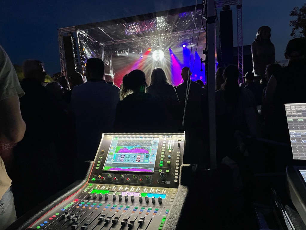 Digital lydmixer ved udendørs koncert om aftenen med publikum og scenelys